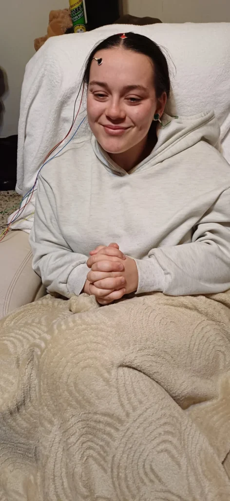 Manon en séance de neurofeedback Cygnet, détendue et souriante, avec des capteurs posés sur la tête et enveloppée dans une couverture.