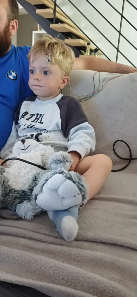 Telio en séance de neurofeedback, assis calmement avec un doudou, des capteurs posés sur la tête, accompagné d’un adulte.
